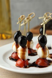 Photo of Tasty canapes with black olives, mozzarella and cherry tomatoes on light wooden table, closeup