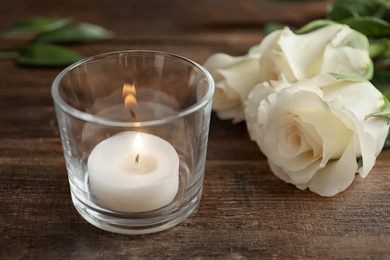 Photo of Glass with burning wax candle near flowers on wooden table