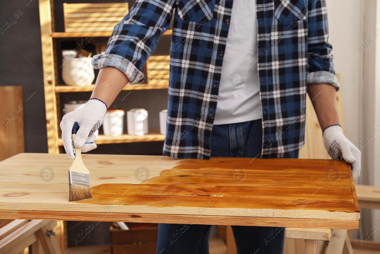 Photo of Man with brush applying wood stain onto wooden surface indoors, closeup