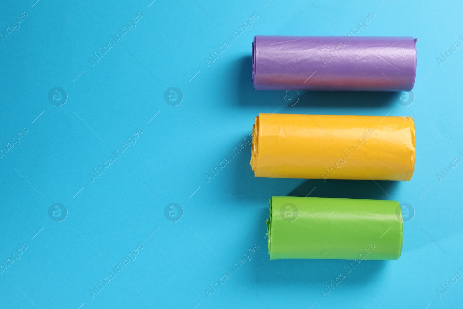 Photo of Rolls of different garbage bags on light blue background, flat lay. Space for text