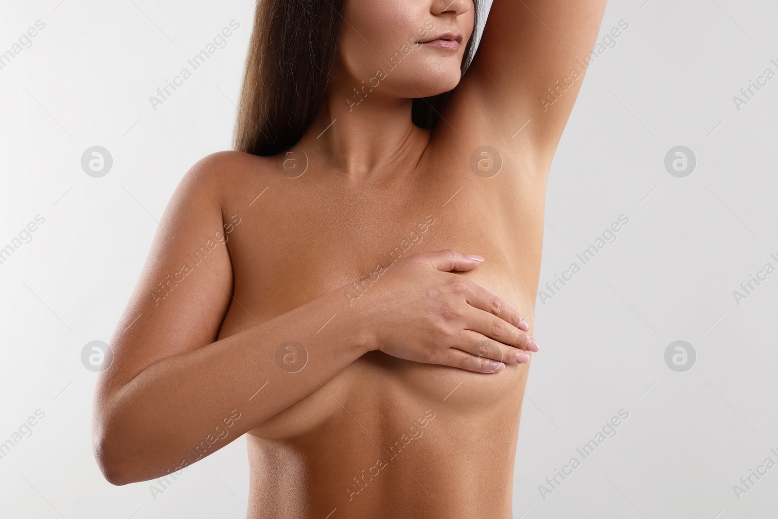 Photo of Naked woman covering her breast on light grey background, closeup