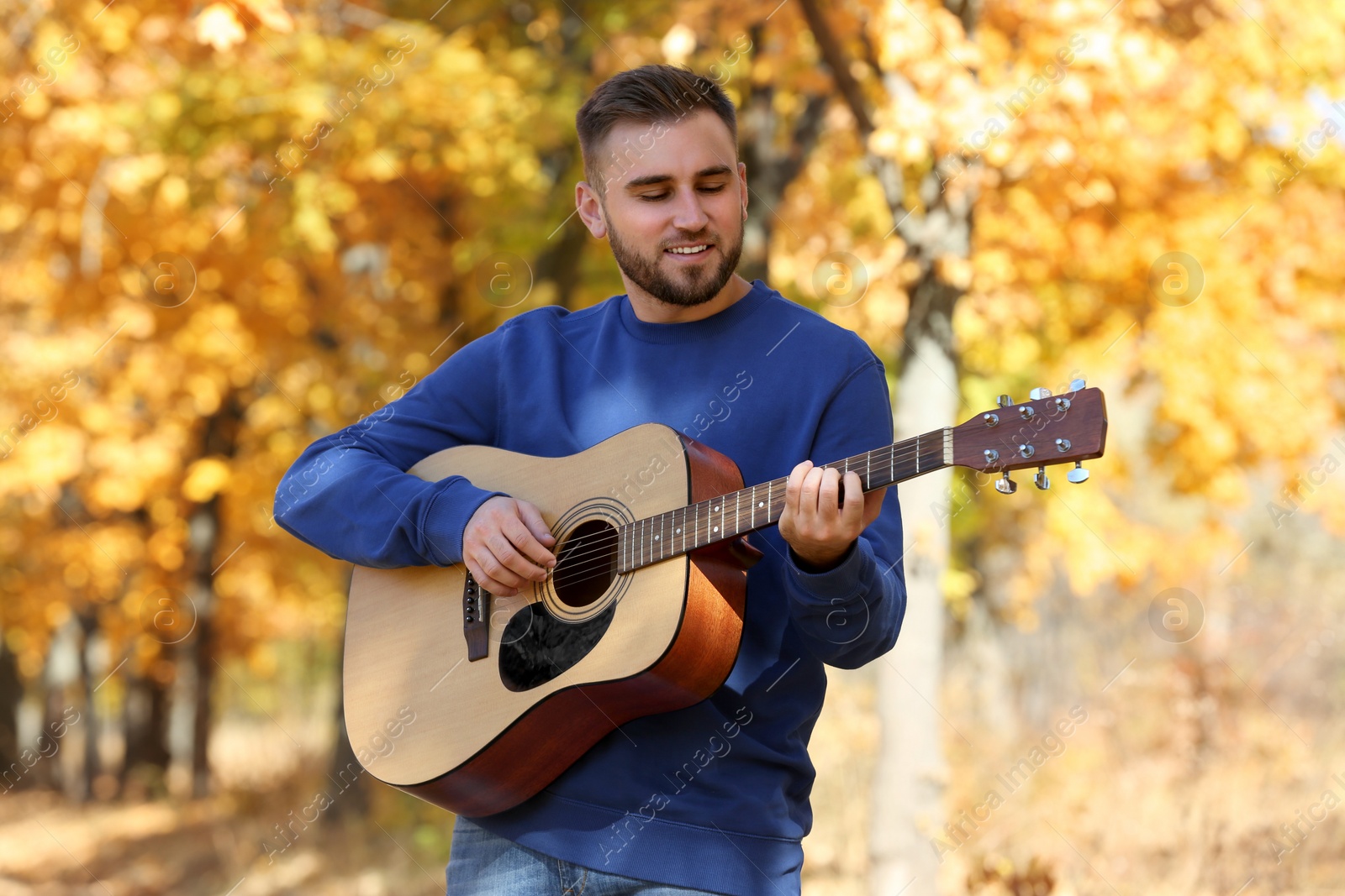 Photo of Young man with acoustic guitar in autumn park