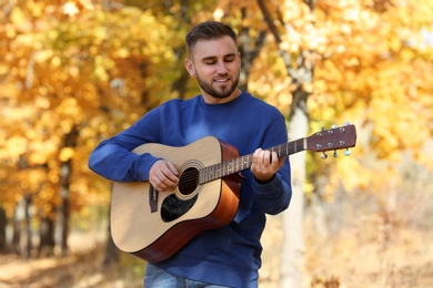 Young man with acoustic guitar in autumn park