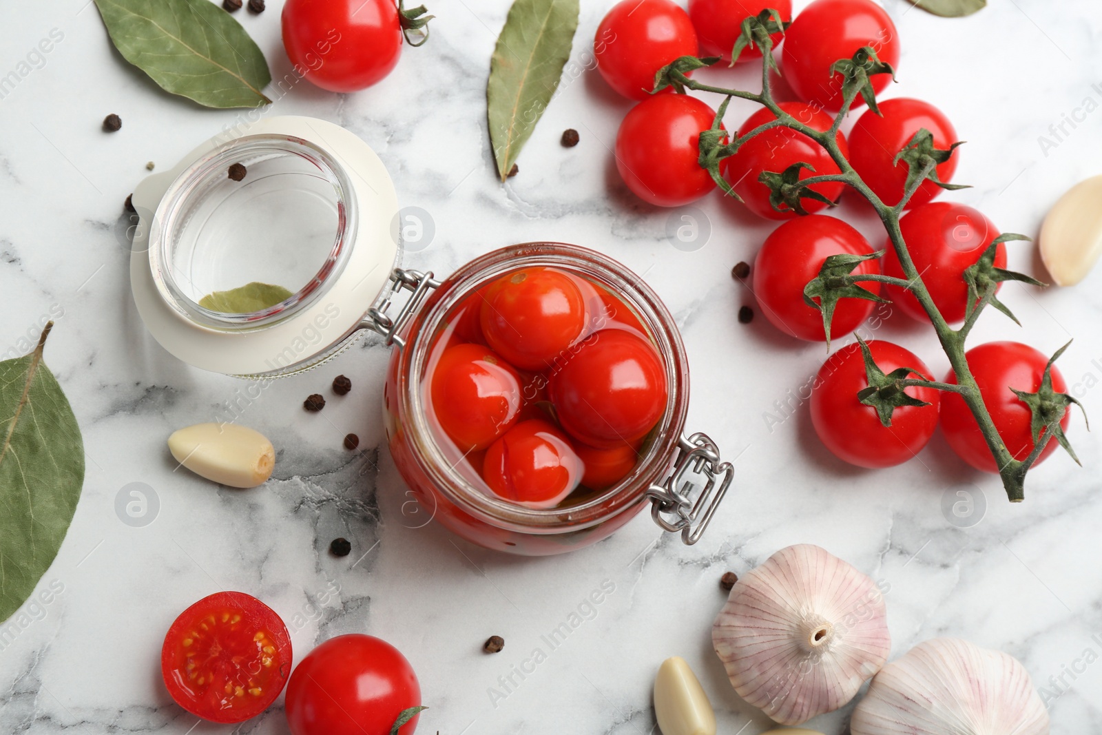 Photo of Glass jar of pickled cherry tomatoes on white marble table, flat lay