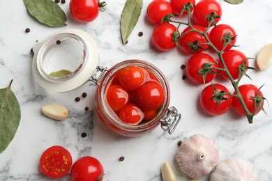Photo of Glass jar of pickled cherry tomatoes on white marble table, flat lay