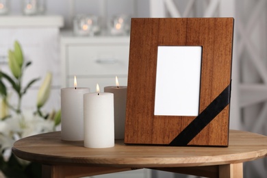 Photo of Funeral photo frame with black ribbon and burning candles on table, indoors