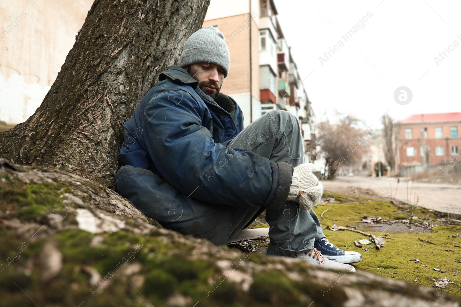 Photo of Poor homeless man sitting on ground outdoors