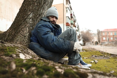 Photo of Poor homeless man sitting on ground outdoors