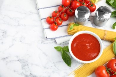 Flat lay composition with bowl of sauce, pasta and tomatoes on marble table. Space for text