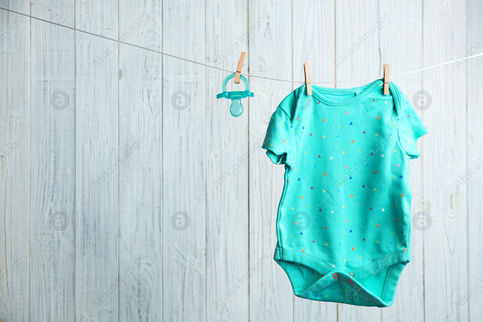 Photo of Baby accessories on laundry line against wooden background. Space for text