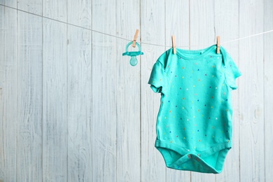 Baby accessories on laundry line against wooden background. Space for text