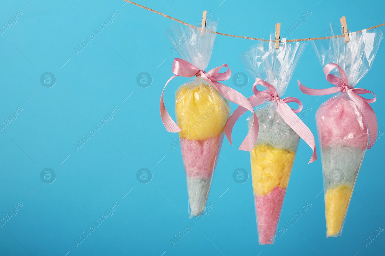 Photo of Packaged sweet cotton candies hanging on clothesline against light blue background, space for text