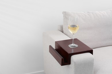 Photo of Glass of white wine on sofa with wooden armrest table indoors, space for text. Interior element