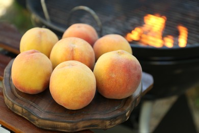 Fresh peaches on wooden board near modern grill outdoors, closeup