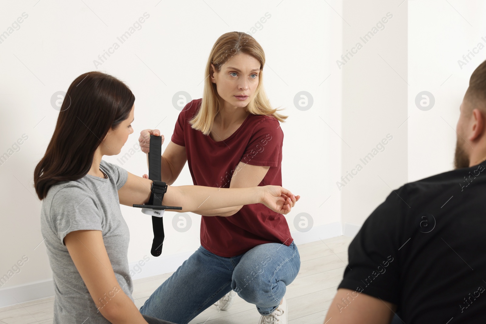 Photo of Group of people learning how to apply medical tourniquet on arm indoors