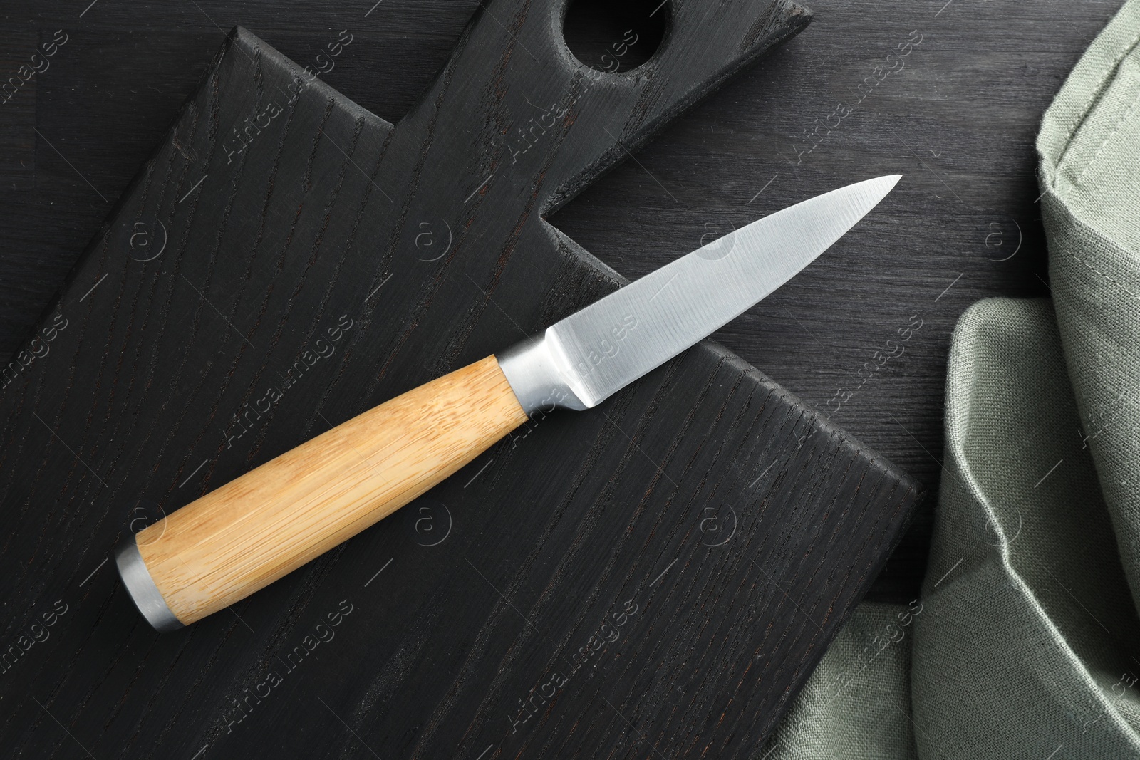 Photo of One sharp knife, cloth and board on black wooden table, top view