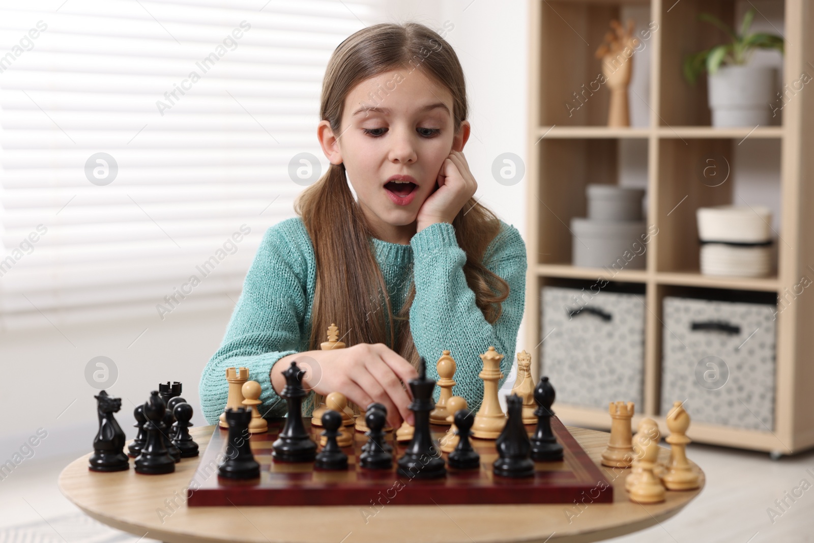 Photo of Cute girl playing chess at table in room