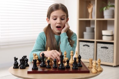 Photo of Cute girl playing chess at table in room