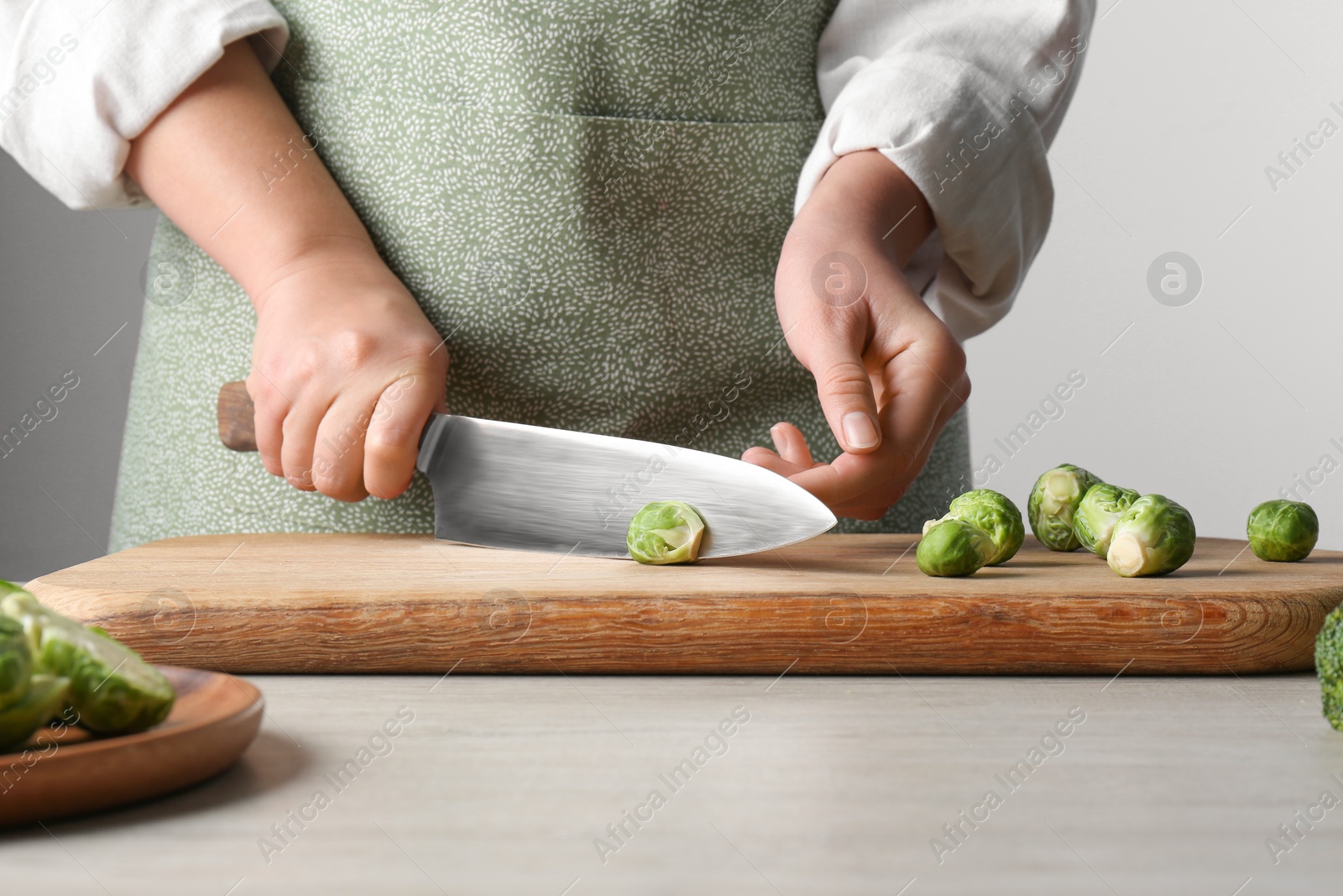 Photo of Woman cutting fresh brussel sprouts on board at wooden table, closeup