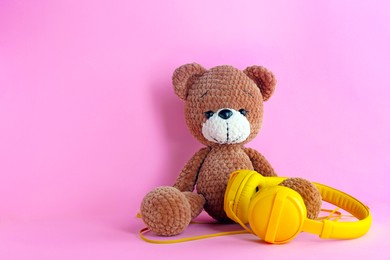 Photo of Baby songs. Toy bear and yellow headphones on pink background, space for text