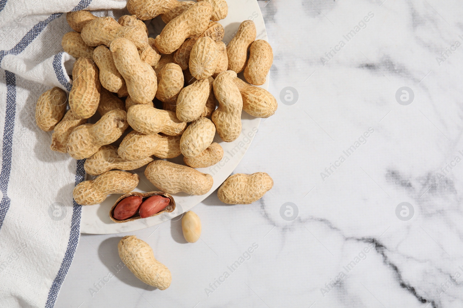 Photo of Fresh unpeeled peanuts on white marble table, top view. Space for text