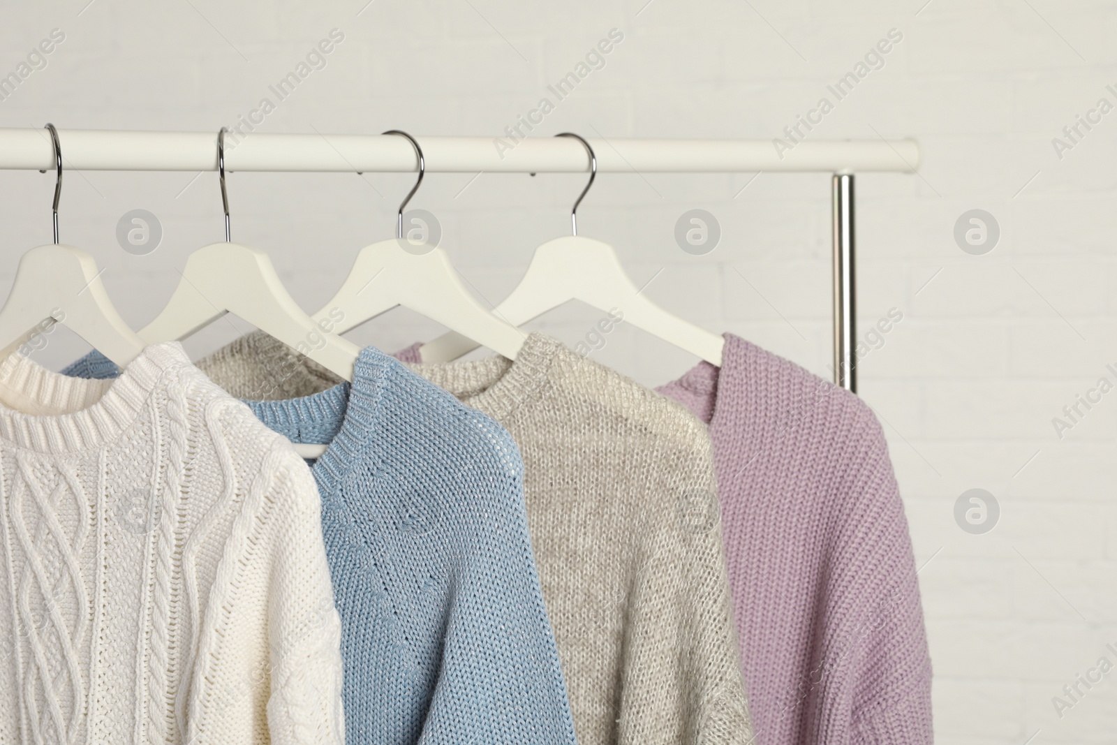 Photo of Collection of warm sweaters hanging on rack against white brick wall