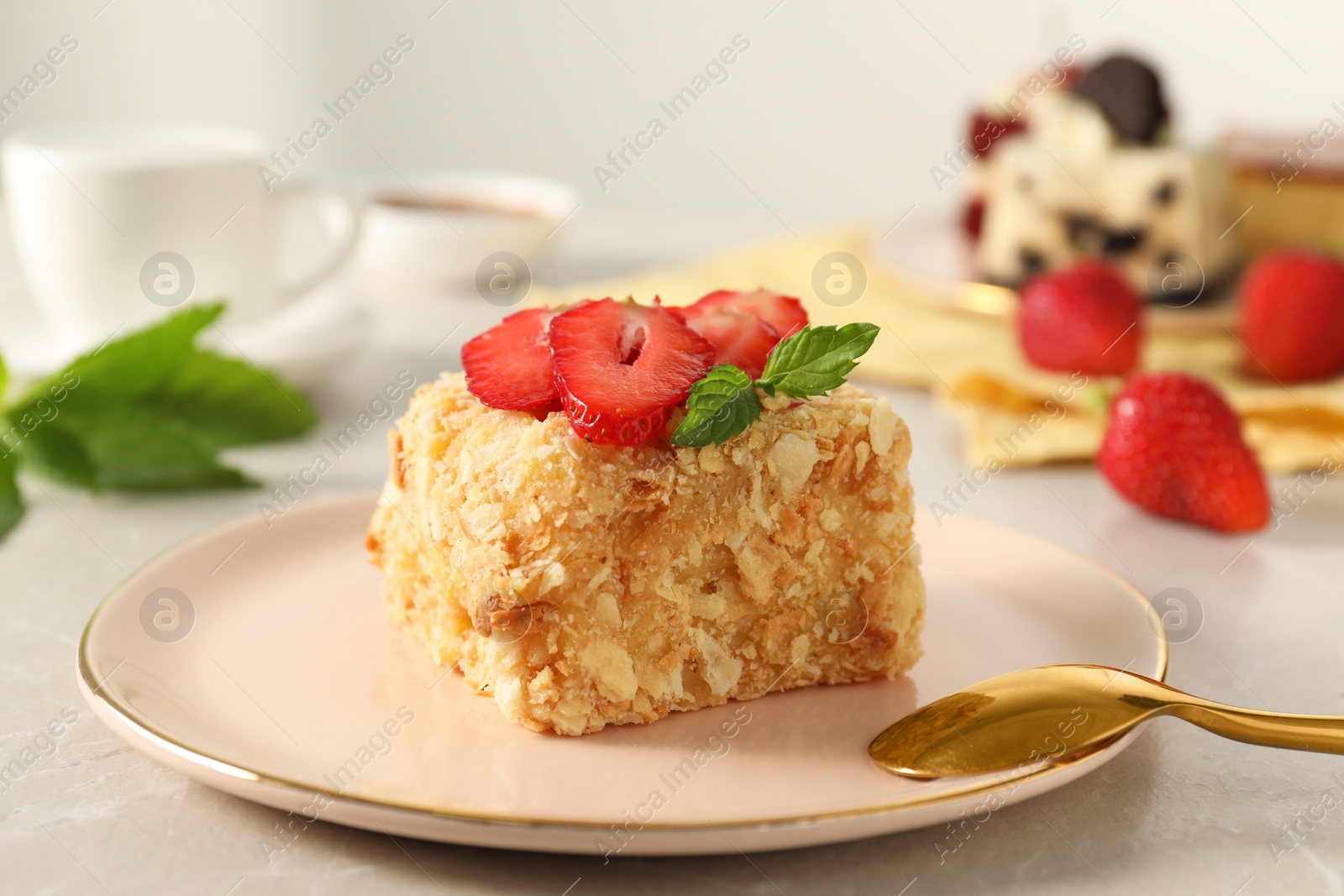 Photo of Piece of delicious Napoleon cake with fresh strawberries on light grey table, closeup