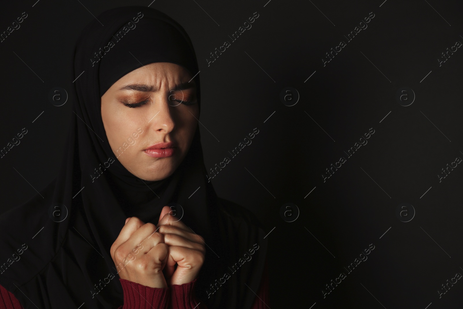 Photo of Portrait of sad Muslim woman in hijab  praying on dark background. Space for text