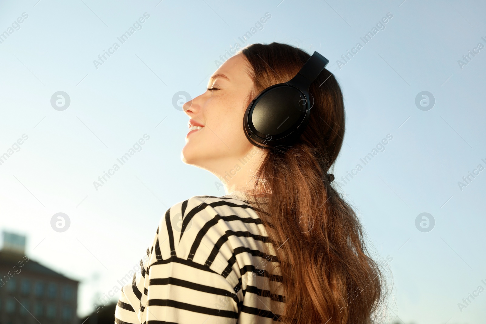 Photo of Smiling woman in headphones listening to music outdoors