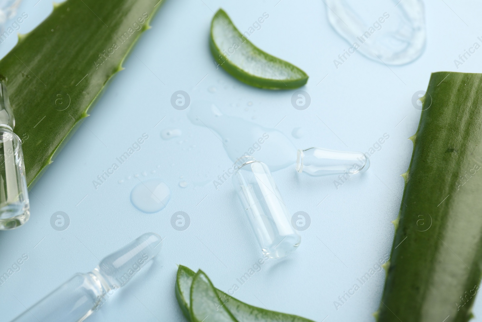 Photo of Skincare ampoules with extract of aloe vera and green leaves on light blue background, closeup