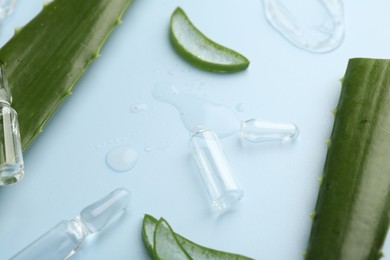 Skincare ampoules with extract of aloe vera and green leaves on light blue background, closeup