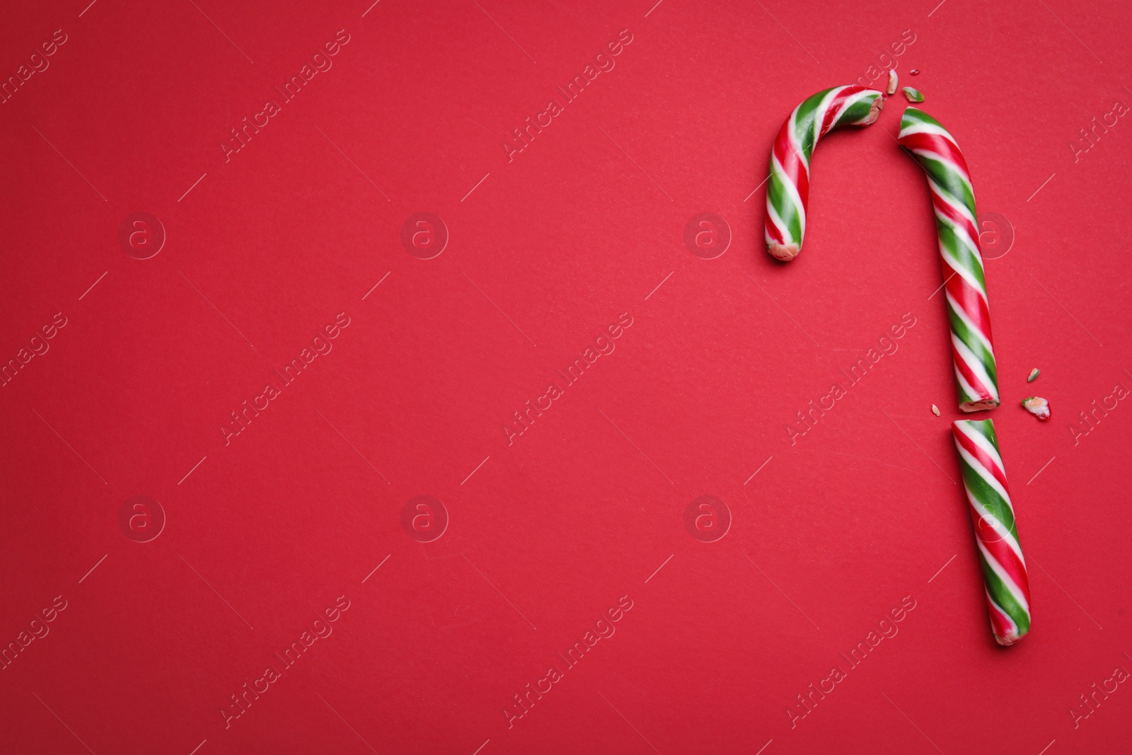 Photo of Broken sweet Christmas candy cane on red background, top view. Space for text