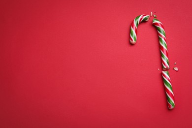 Photo of Broken sweet Christmas candy cane on red background, top view. Space for text