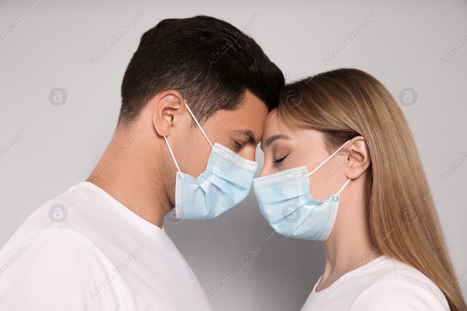 Photo of Couple in medical masks trying to kiss on light background