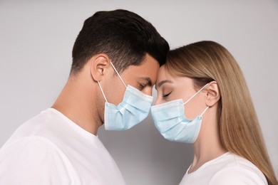 Couple in medical masks trying to kiss on light background