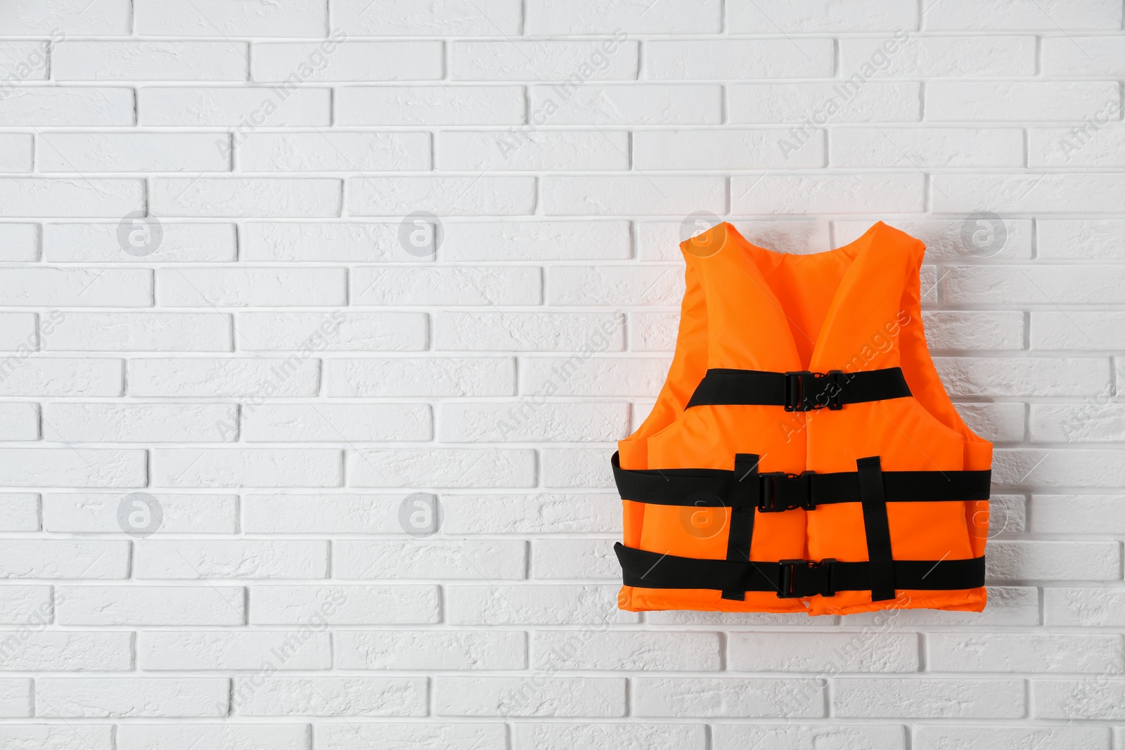 Photo of Orange life jacket on white brick wall. Space for text