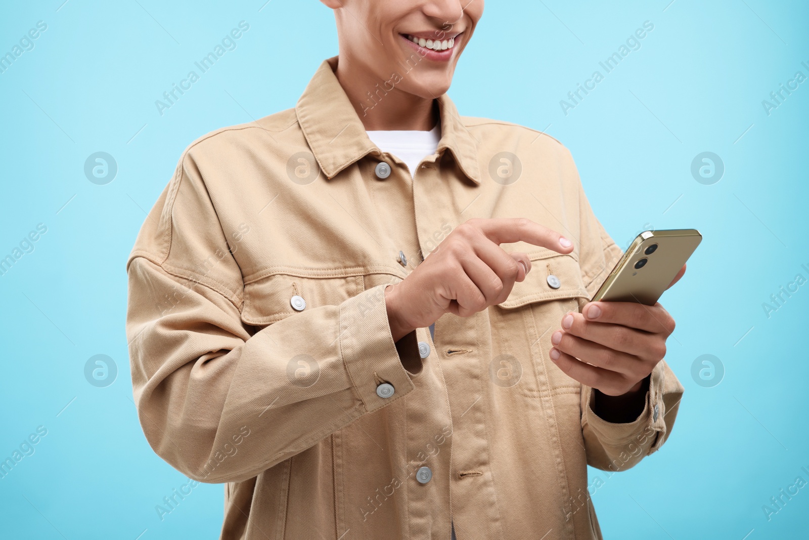 Photo of Young man sending message via smartphone on light blue background, closeup