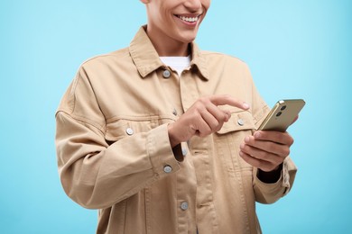 Photo of Young man sending message via smartphone on light blue background, closeup