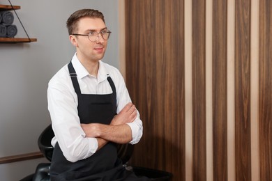 Photo of Professional hairdresser wearing apron in beauty salon, space for text