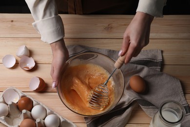 Woman whisking eggs in bowl at wooden table, above view