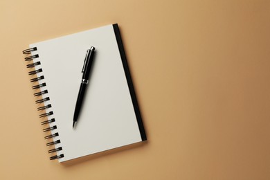 Photo of Notebook and pen on beige background, top view. Space for text