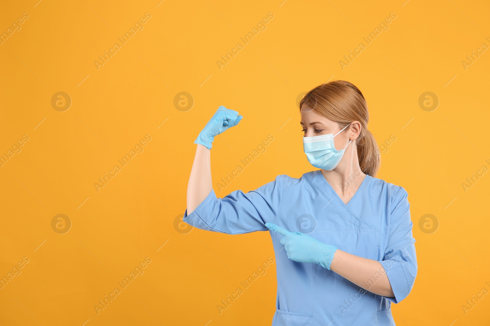 Photo of Doctor with protective mask showing muscles on yellow background, space for text. Strong immunity concept