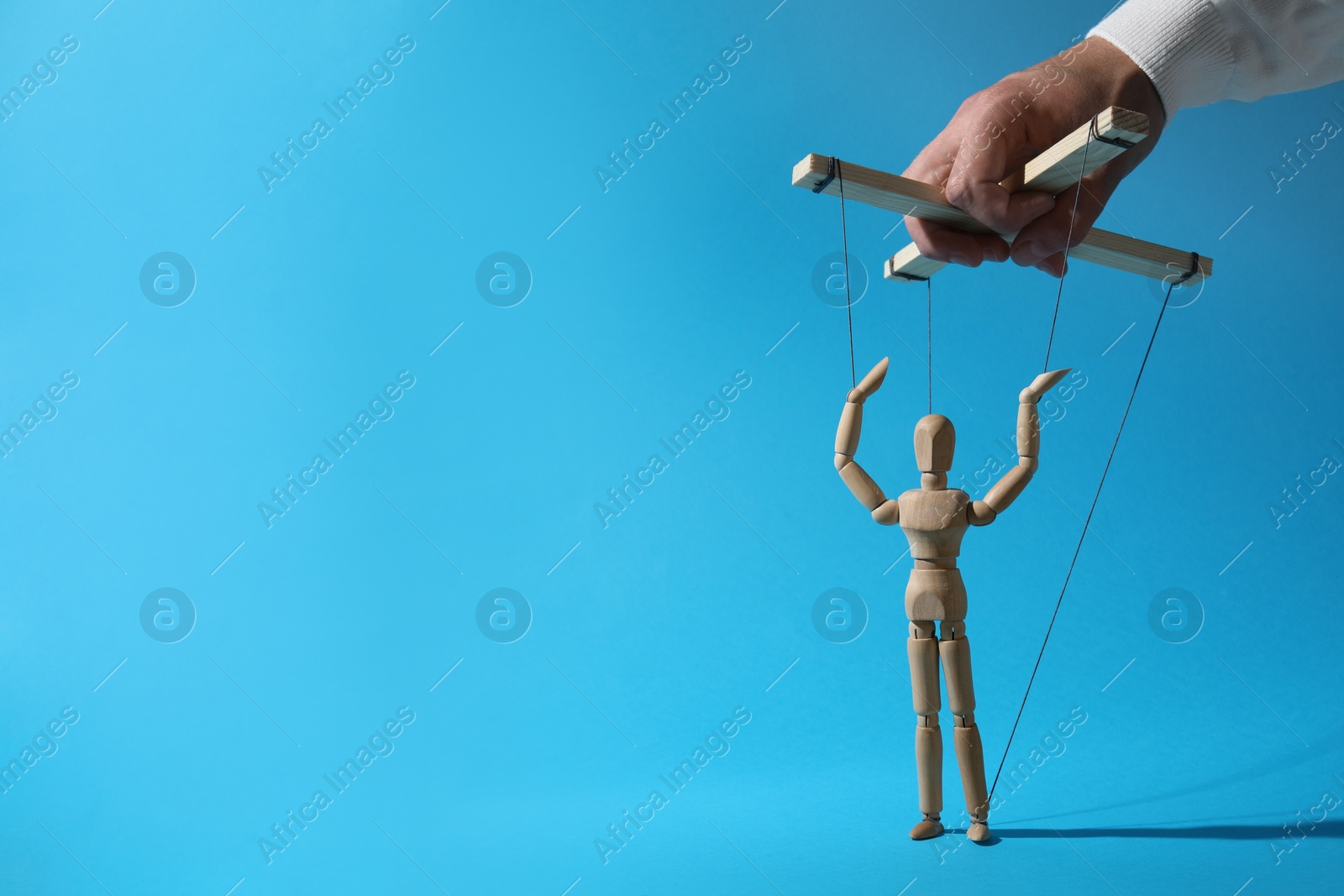 Photo of Man pulling strings of puppet on light blue background, closeup. Space for text
