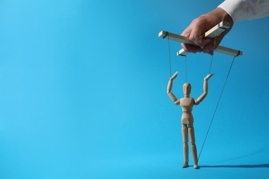 Man pulling strings of puppet on light blue background, closeup. Space for text