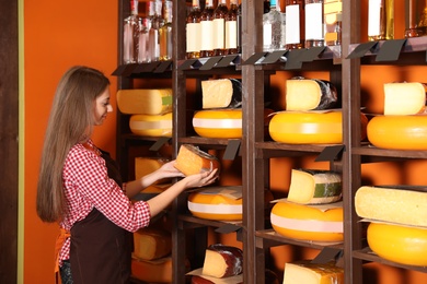 Photo of Seller with piece of delicious cheese near rack in store