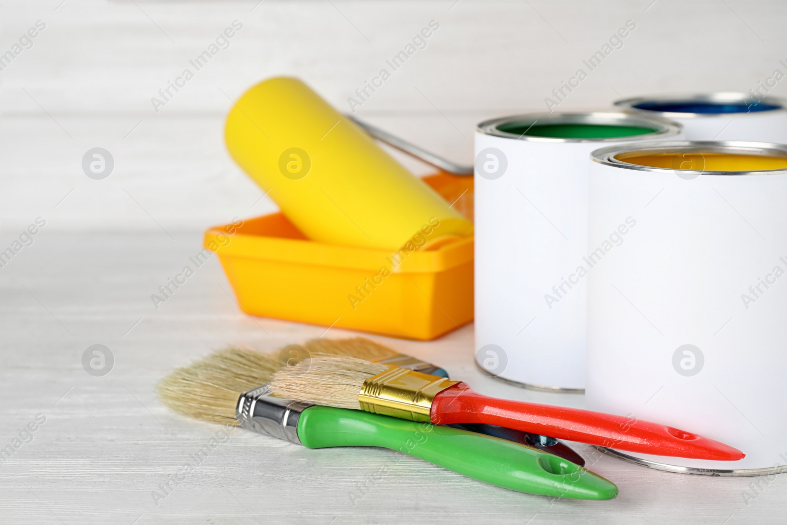 Photo of Cans of paint and brushes on white wooden table. Space for text