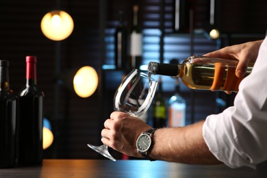 Photo of Man pouring white wine into glass indoors, closeup