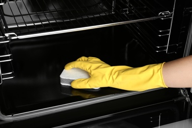 Woman cleaning electric oven with sponge, closeup