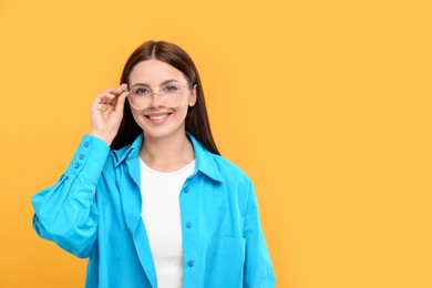 Portrait of smiling woman in stylish eyeglasses on orange background. Space for text