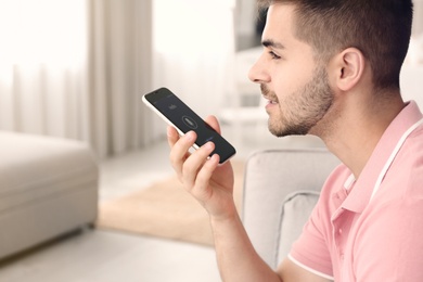 Photo of Young man using voice search on smartphone indoors